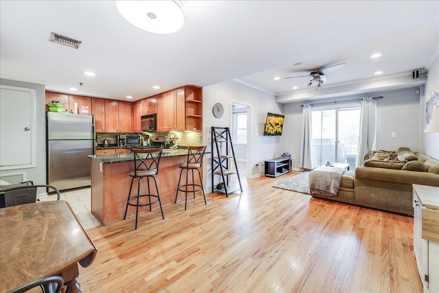 kitchen with a breakfast bar, light wood-type flooring, stainless steel refrigerator, ornamental molding, and backsplash