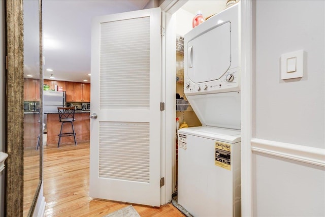 clothes washing area with stacked washer / drying machine and light wood-type flooring