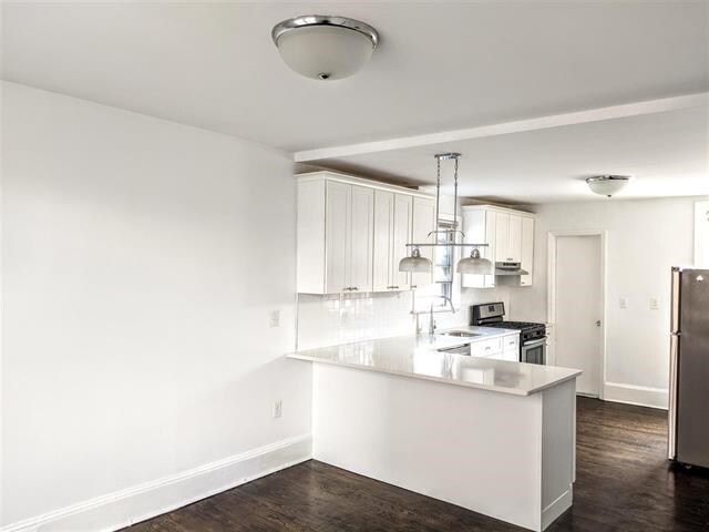 149 37th St, Union City, NJ 07087 - kitchen with appliances with stainless steel finishes, a sink, white cabinets, dark wood-style flooring, and a peninsula