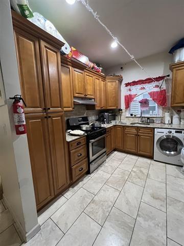 149 37th St, Union City, NJ 07087 - kitchen featuring washer / clothes dryer, electric range, under cabinet range hood, brown cabinetry, and a sink