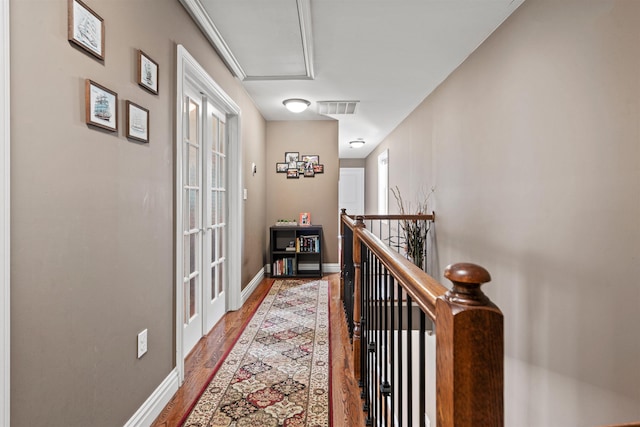 hall with attic access, baseboards, an upstairs landing, wood finished floors, and visible vents