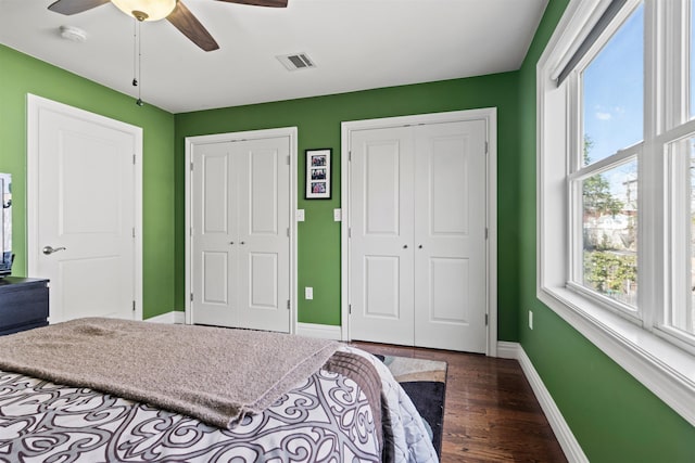 bedroom with baseboards, multiple windows, two closets, and dark wood-style flooring