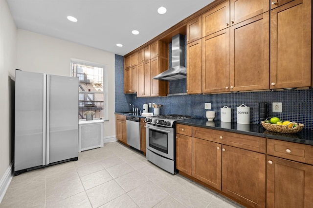 kitchen with appliances with stainless steel finishes, dark countertops, brown cabinets, and wall chimney range hood