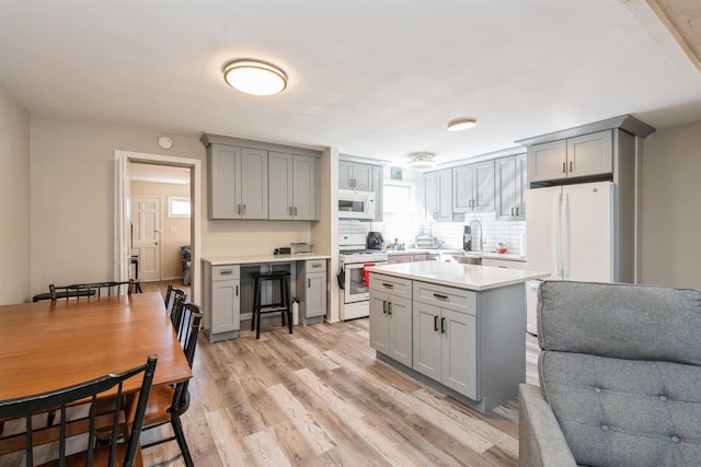 kitchen featuring white appliances, light countertops, a sink, and gray cabinetry