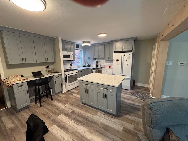 kitchen with gray cabinets, light countertops, a sink, wood finished floors, and white appliances