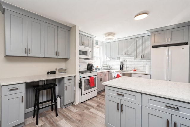 kitchen with gray cabinets, light wood-style flooring, decorative backsplash, light stone countertops, and white appliances