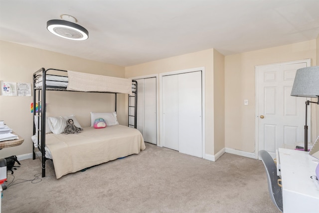 bedroom featuring baseboards, two closets, and light colored carpet