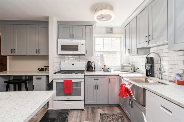 kitchen with light wood finished floors, white appliances, decorative backsplash, and gray cabinetry