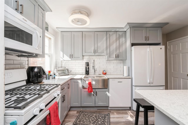 kitchen featuring white appliances, backsplash, gray cabinets, and a sink