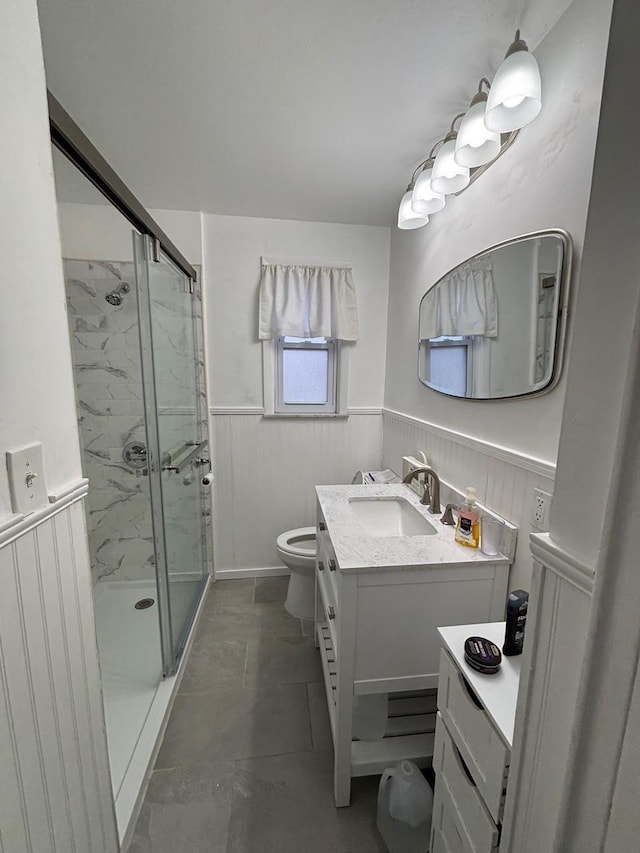 bathroom featuring toilet, wainscoting, a marble finish shower, and vanity