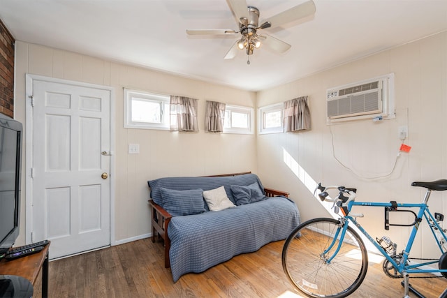 sitting room with a ceiling fan, wood finished floors, and a wall mounted air conditioner