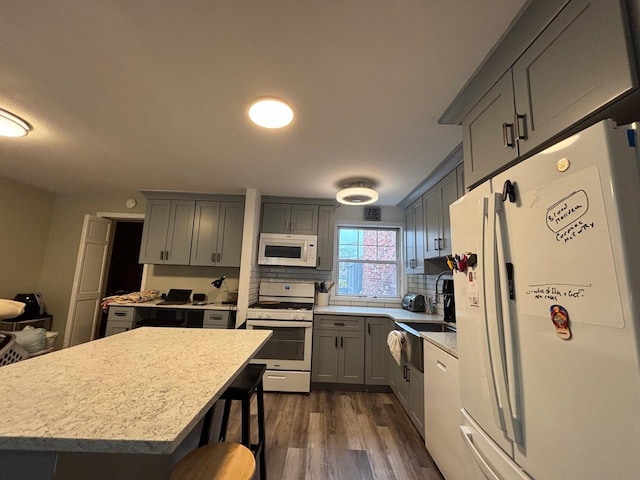 kitchen with a breakfast bar area, gray cabinets, light countertops, dark wood-type flooring, and white appliances