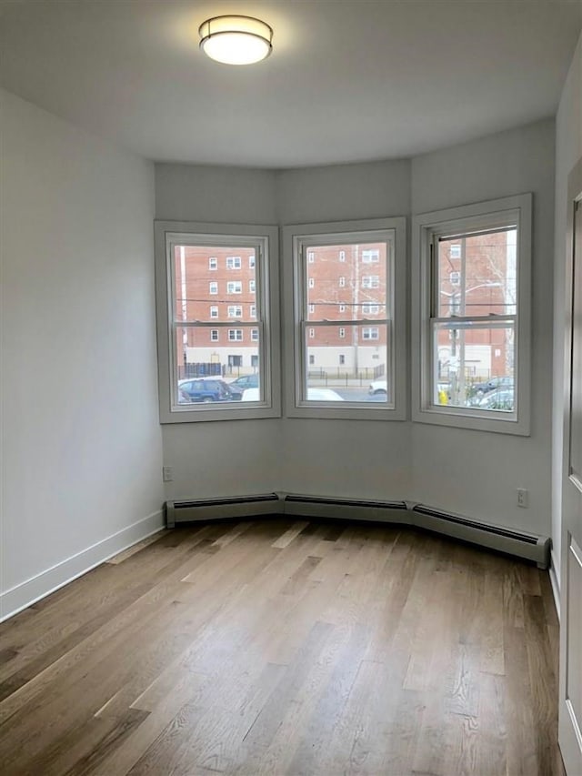 24 E 49th St, Bayonne, NJ 07002 - empty room featuring a baseboard heating unit, wood finished floors, and baseboards