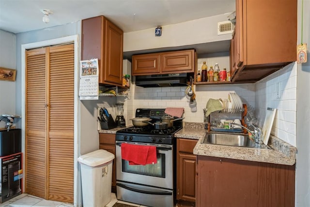 kitchen featuring light tile patterned floors, stainless steel gas range oven, sink, and tasteful backsplash