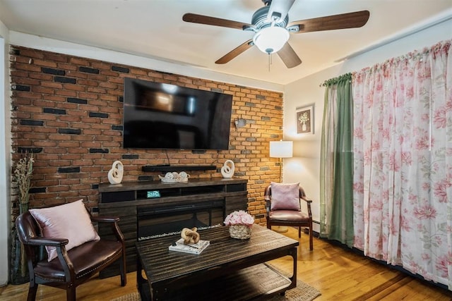 living area featuring a fireplace, light hardwood / wood-style floors, ceiling fan, and brick wall