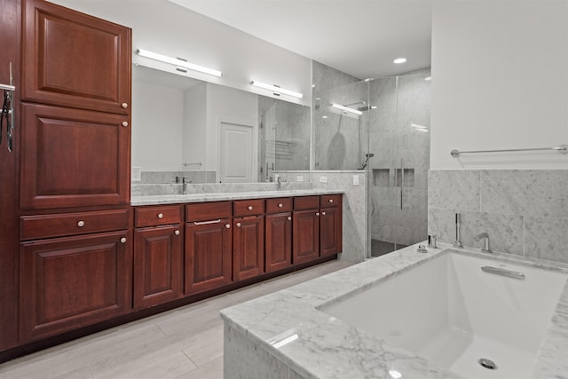 bathroom featuring a shower stall, double vanity, tile walls, a bath, and a sink