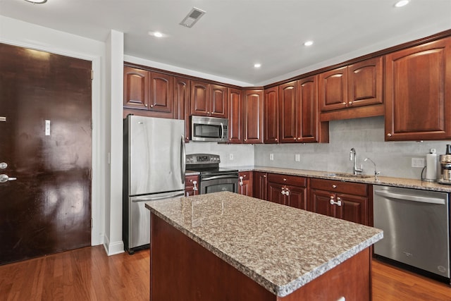 kitchen featuring dark wood finished floors, stainless steel appliances, a center island, a sink, and visible vents