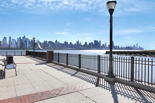 view of patio / terrace featuring a view of city, a water view, and fence