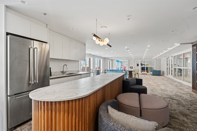 kitchen featuring carpet, high quality fridge, a sink, white cabinetry, and open floor plan