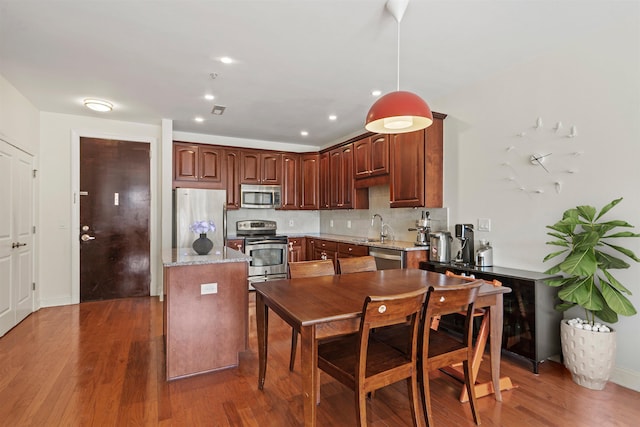 kitchen featuring decorative backsplash, a sink, appliances with stainless steel finishes, decorative light fixtures, and wood finished floors