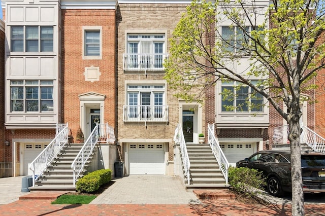 townhome / multi-family property featuring a garage, decorative driveway, stairway, and brick siding