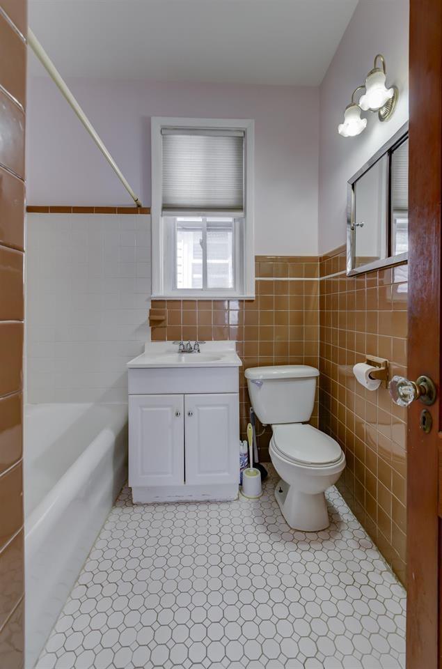 full bathroom featuring toilet, tile walls, wainscoting, tub / shower combination, and vanity