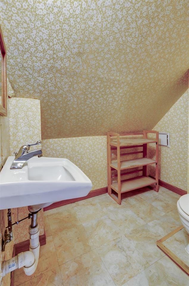 half bathroom with toilet, wallpapered walls, baseboards, and a sink