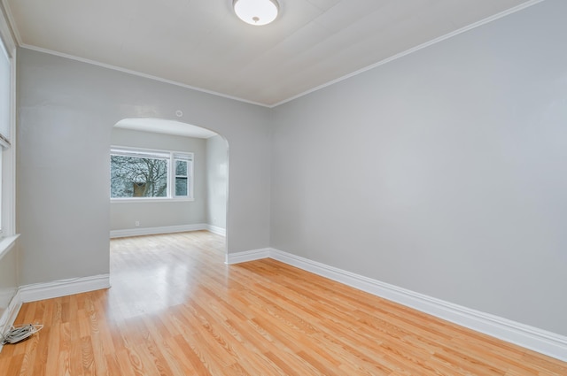 empty room with arched walkways, crown molding, baseboards, and wood finished floors