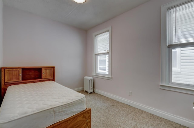 bedroom with light colored carpet, radiator heating unit, and baseboards