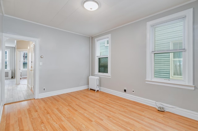 empty room with light wood-style flooring, radiator, crown molding, and baseboards