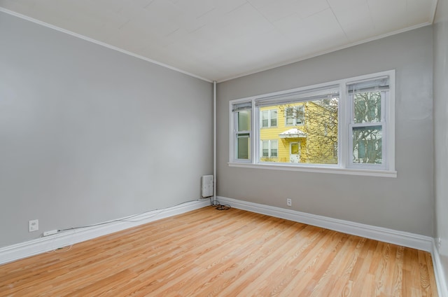 empty room with baseboards, light wood-type flooring, and ornamental molding