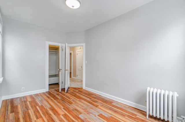 unfurnished bedroom with a closet, radiator, light wood-type flooring, and baseboards