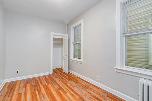 unfurnished bedroom featuring radiator heating unit, light wood-style floors, baseboards, and a closet