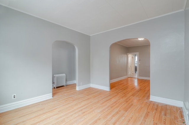 empty room featuring light wood-style flooring, radiator, baseboards, and arched walkways