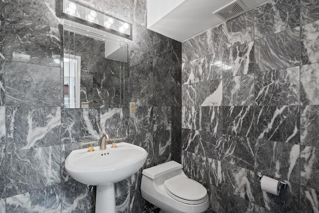 half bath featuring tile walls, toilet, and visible vents