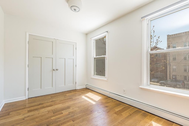 unfurnished bedroom with multiple windows, a baseboard radiator, light hardwood / wood-style flooring, and a closet