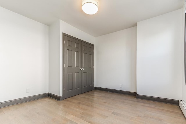 unfurnished bedroom featuring a closet, a baseboard heating unit, and light wood-type flooring