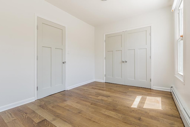 unfurnished bedroom featuring hardwood / wood-style flooring, baseboard heating, and a closet