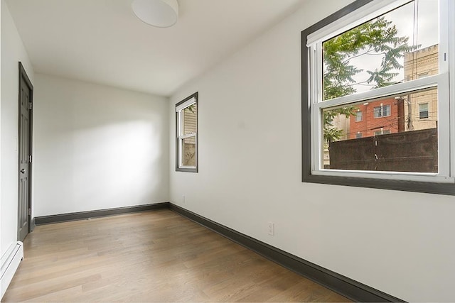 empty room featuring light wood-type flooring and a baseboard heating unit