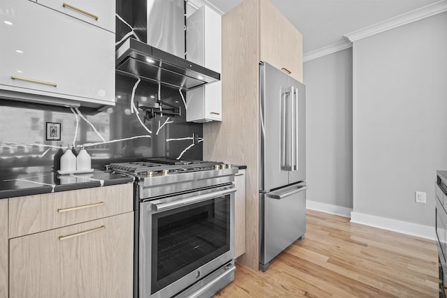 kitchen featuring wall chimney exhaust hood, light brown cabinetry, appliances with stainless steel finishes, and tasteful backsplash