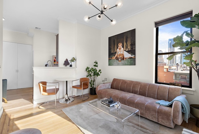 living room with sink, light wood-type flooring, ornamental molding, and an inviting chandelier