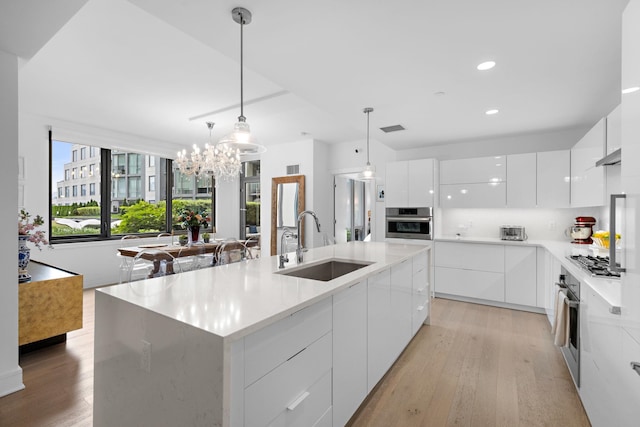 kitchen with white cabinets, sink, an island with sink, appliances with stainless steel finishes, and decorative light fixtures