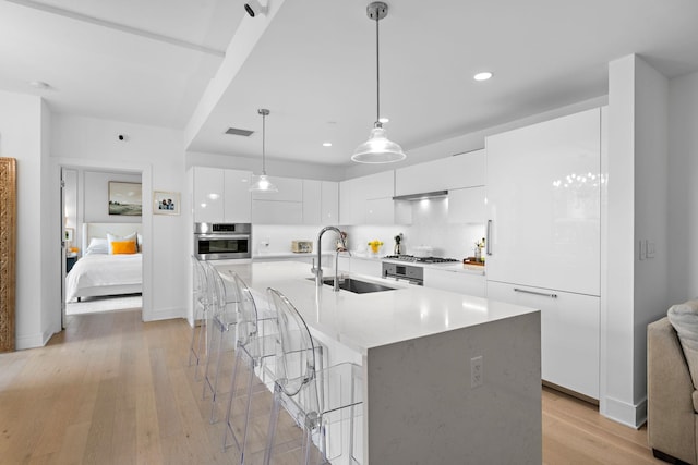 kitchen featuring stainless steel oven, sink, light hardwood / wood-style floors, and white cabinets