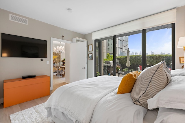 bedroom featuring access to exterior, light wood-type flooring, and a notable chandelier