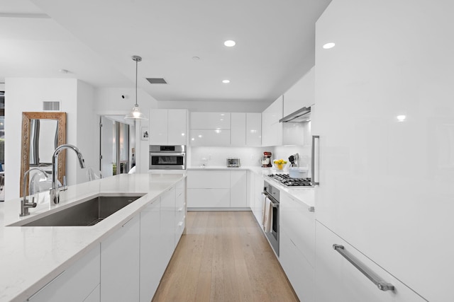 kitchen with sink, appliances with stainless steel finishes, decorative light fixtures, light hardwood / wood-style flooring, and white cabinets