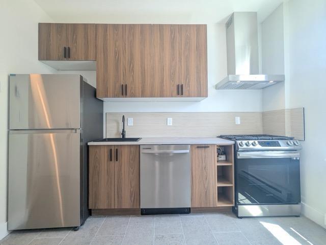368 Palisade Ave, Jersey City, NJ 07307 - kitchen featuring stainless steel appliances, wall chimney range hood, brown cabinetry, a sink, and backsplash