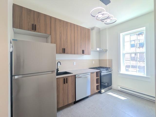 368 Palisade Ave, Jersey City, NJ 07307 - kitchen featuring stainless steel appliances, wall chimney range hood, a baseboard heating unit, a sink, and decorative backsplash