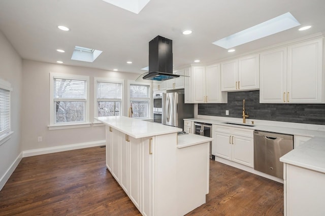 kitchen featuring a skylight, island range hood, white cabinets, stainless steel appliances, and a sink