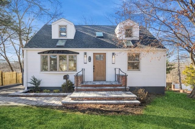 new england style home featuring a front yard, fence, and a shingled roof