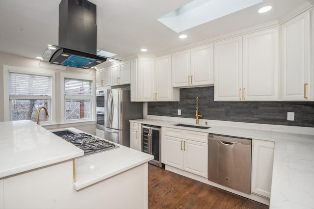 kitchen with a sink, wine cooler, appliances with stainless steel finishes, white cabinets, and island range hood